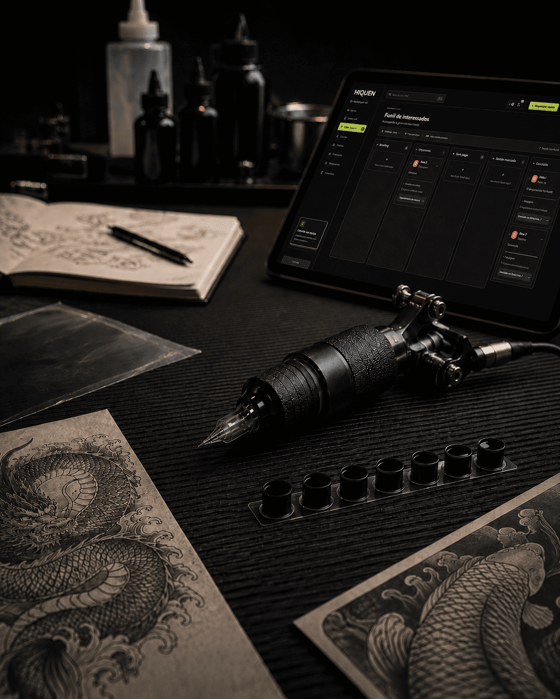 Bancada de tatuagem com máquina, desenhos e tablet exibindo a Hiquen